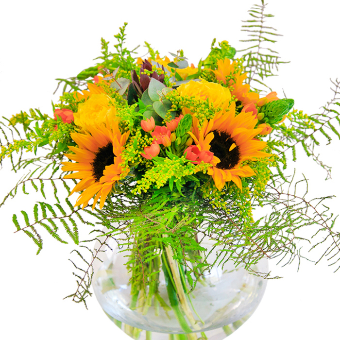 Immediately captivating with its blend of color and texture, this exuberant bouquet from Harold Wood Florist is a tribute to both elegance and local charm. Sunflowers, their faces turned outward as if toward the sun over Harold Wood's green spaces, form the radiant focal point. Encircling them, golden yellow garden roses spiral open in velvety profusion, each petal expertly arranged to maximize visual harmony. Brilliant red hypericum berries glisten among soft, feathery ferns and gentle filler, infusing the bouquet with playful contrast and lively movement. The arrangement is made richer still by slender sprigs of solidago-tiny yellow blossoms echoing the palette of the sunflowers-and dappled sprigs of blue-green eucalyptus that evoke the wild edges of Pages Wood. Carefully cradled in a perfectly rounded, transparent glass vase, the submerged stems appear almost sculptural, reinforcing a sense of deliberate artistry and freshness. Perfect for local celebrations in Harold Wood-birthdays, anniversaries, or special gatherings-this bouquet invites joy and togetherness, capturing all the sunlight and optimism of its home community.